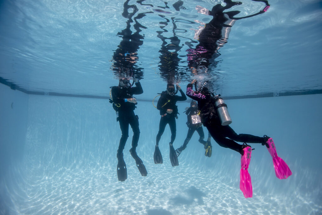 four scuba divers practicing skills underwater in a pool